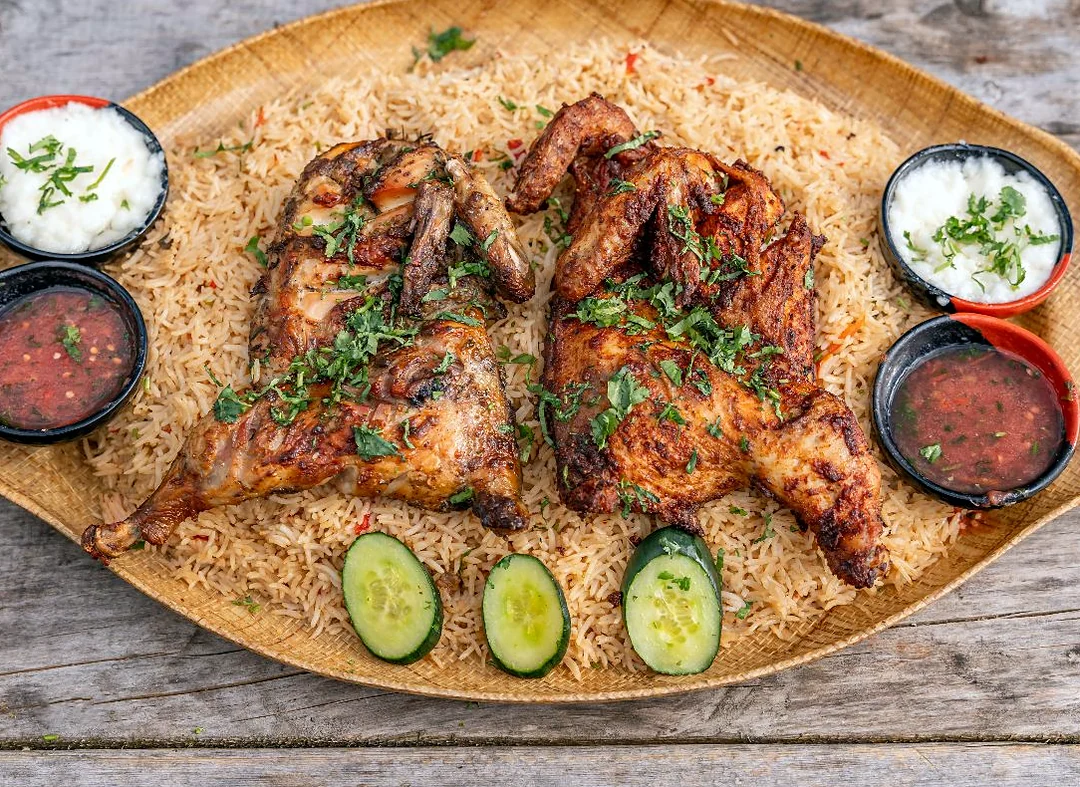 Mandi: two roasted spiced chicken halves on rice with chutneys, garlic sauce and cucumber